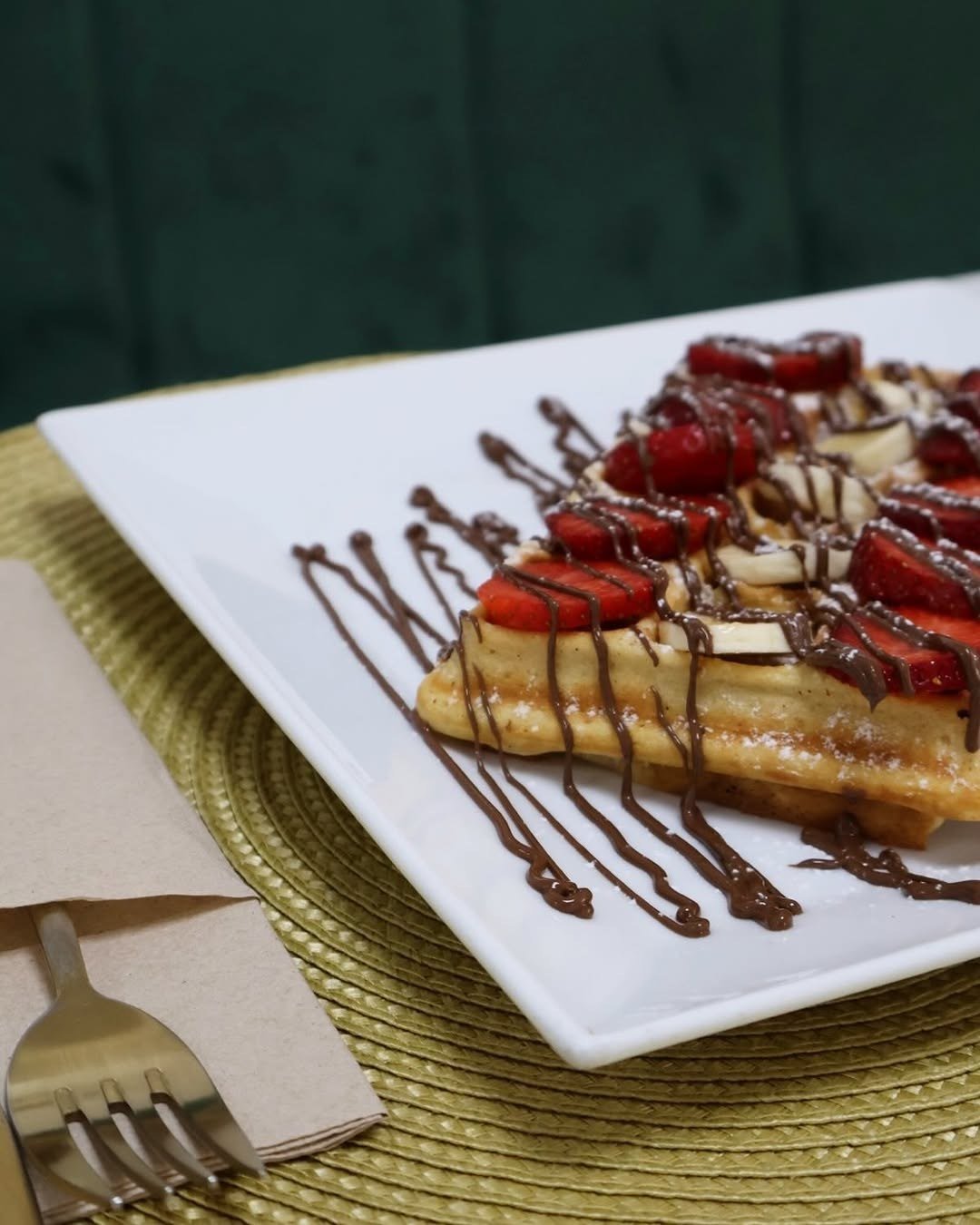 Waffle com morangos, banana e calda de chocolate num prato branco